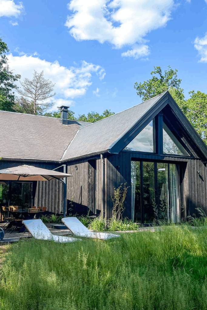 Façade de la Velvet House en bois noir avec grandes baies vitrées et transats design sur la pelouse.