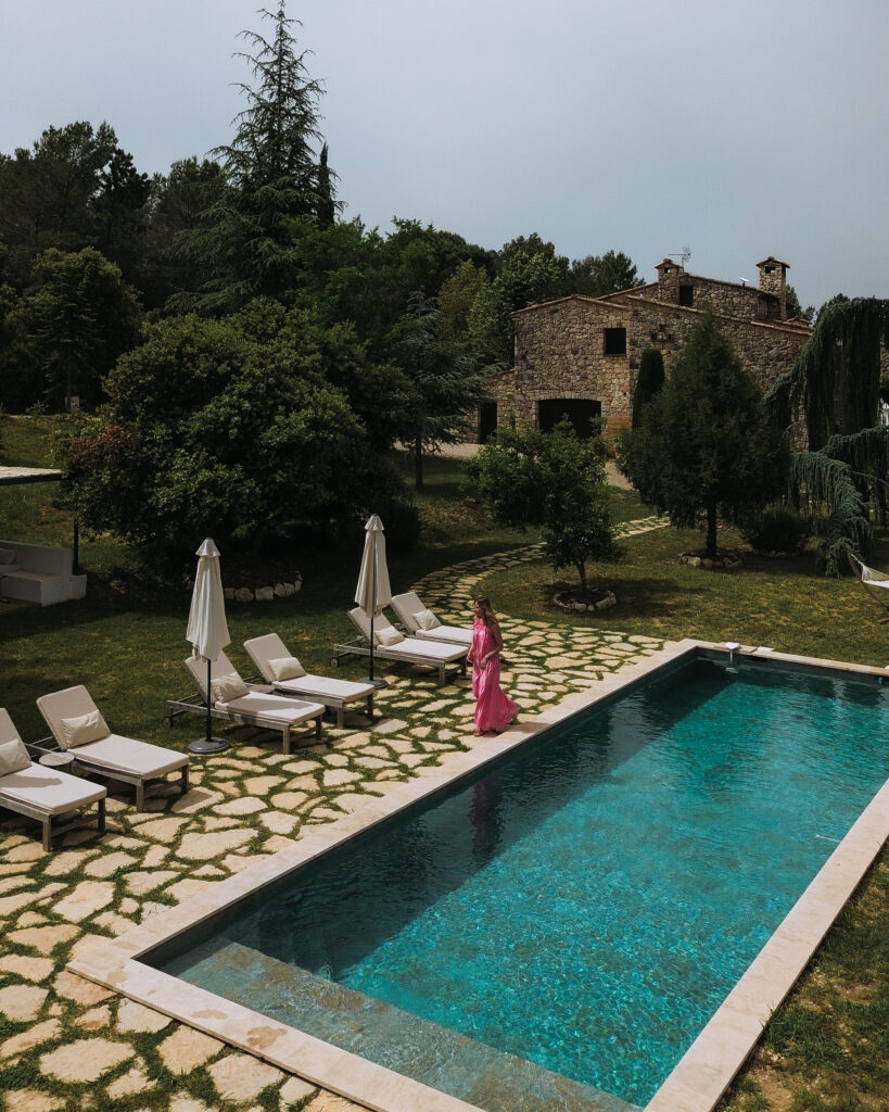 Vue d'ensemble d'un mas provençal en pierre avec jardin paysager, piscine et toit en tuiles anciennes.